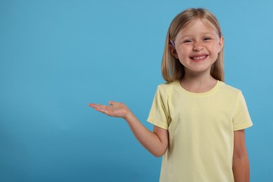 Photo of Special promotion. Little girl showing something on light blue background. Space for text