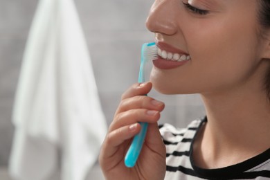 Photo of Young woman brushing her teeth with plastic toothbrush in bathroom, closeup