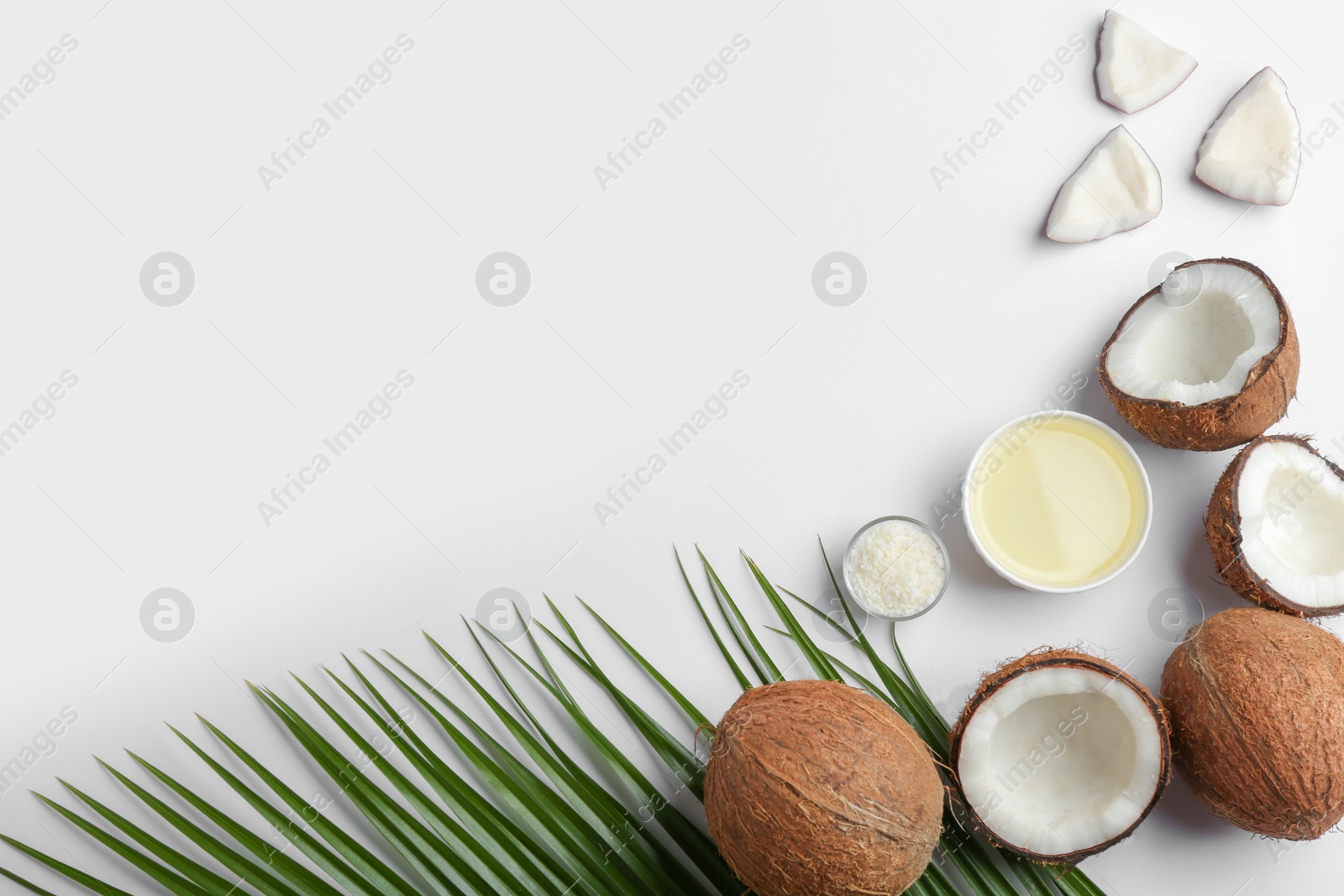 Photo of Bowl of natural organic oil and coconuts on white background, top view. Space for text