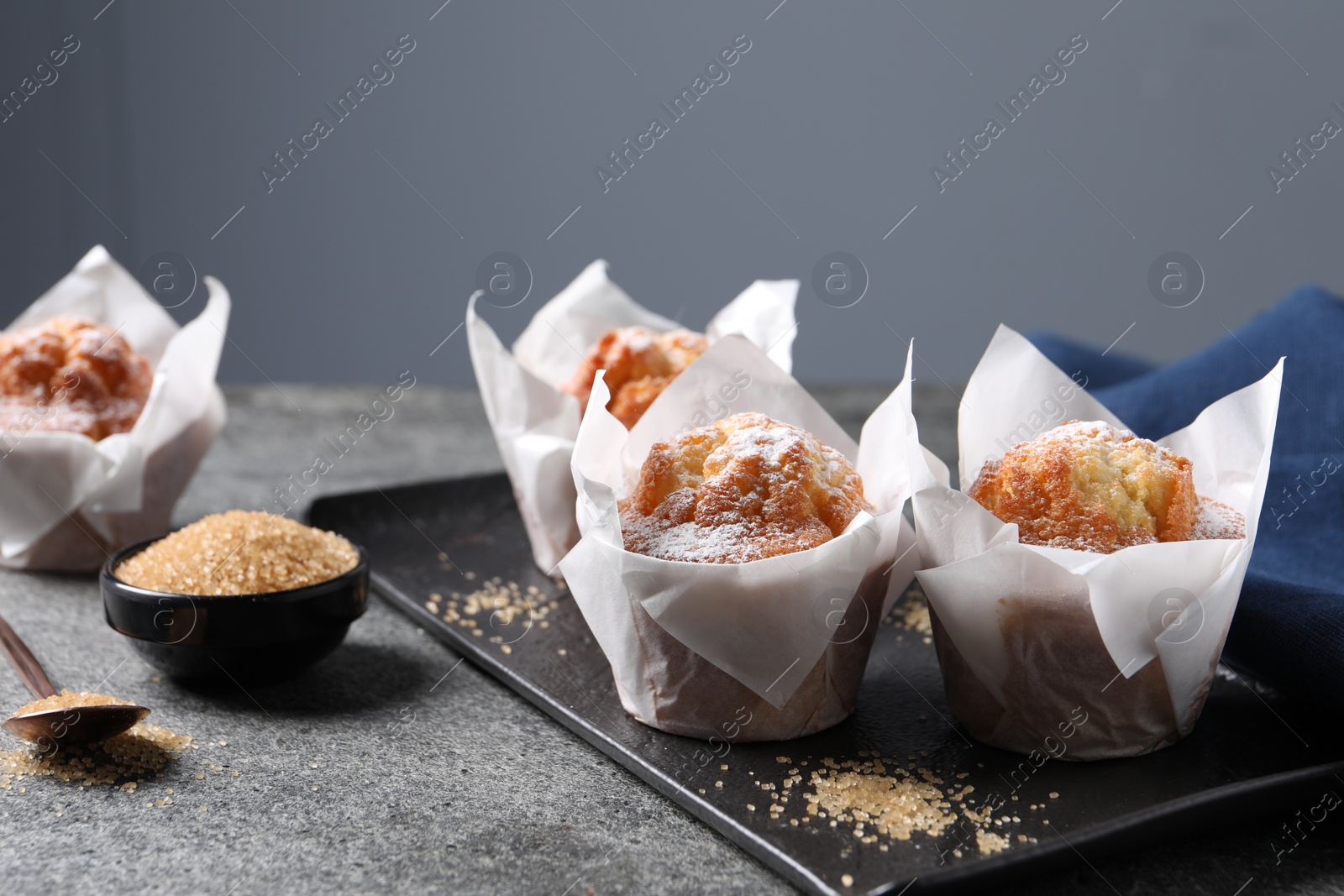 Photo of Delicious muffins with powdered sugar on grey table