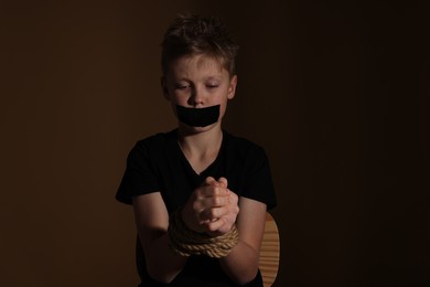 Photo of Little boy with taped mouth tied up and taken hostage against dark background
