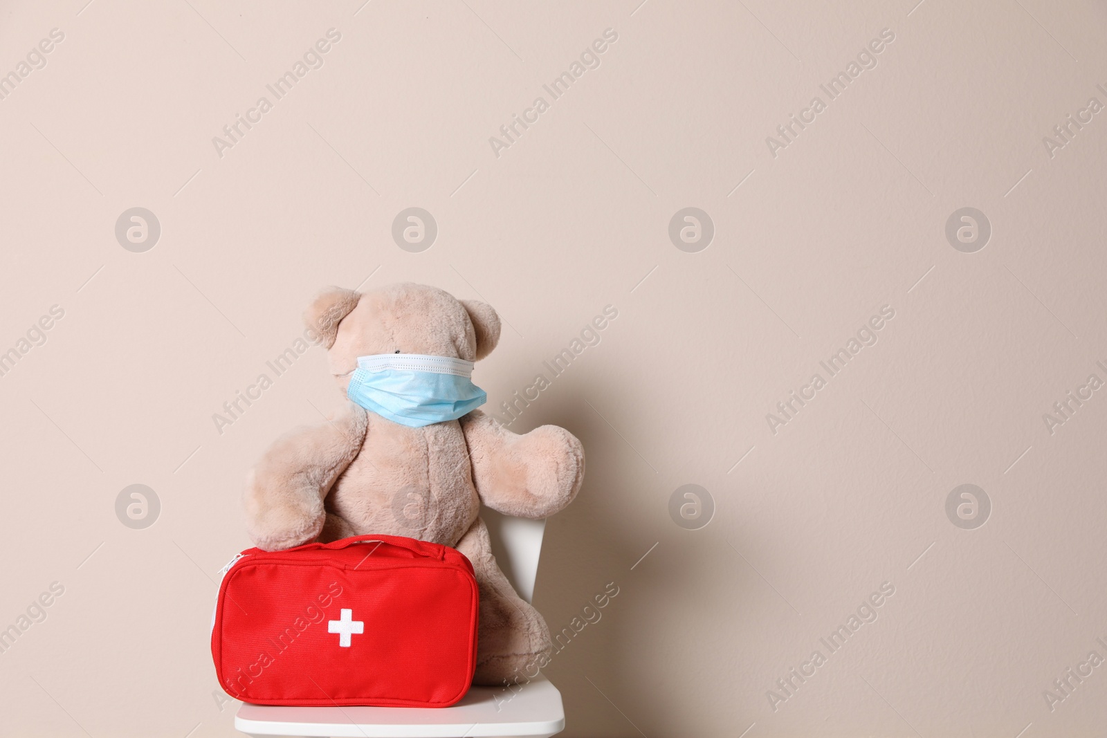Photo of Toy bear with face mask and first aid bag on beige background, space for text. Pediatrician practice