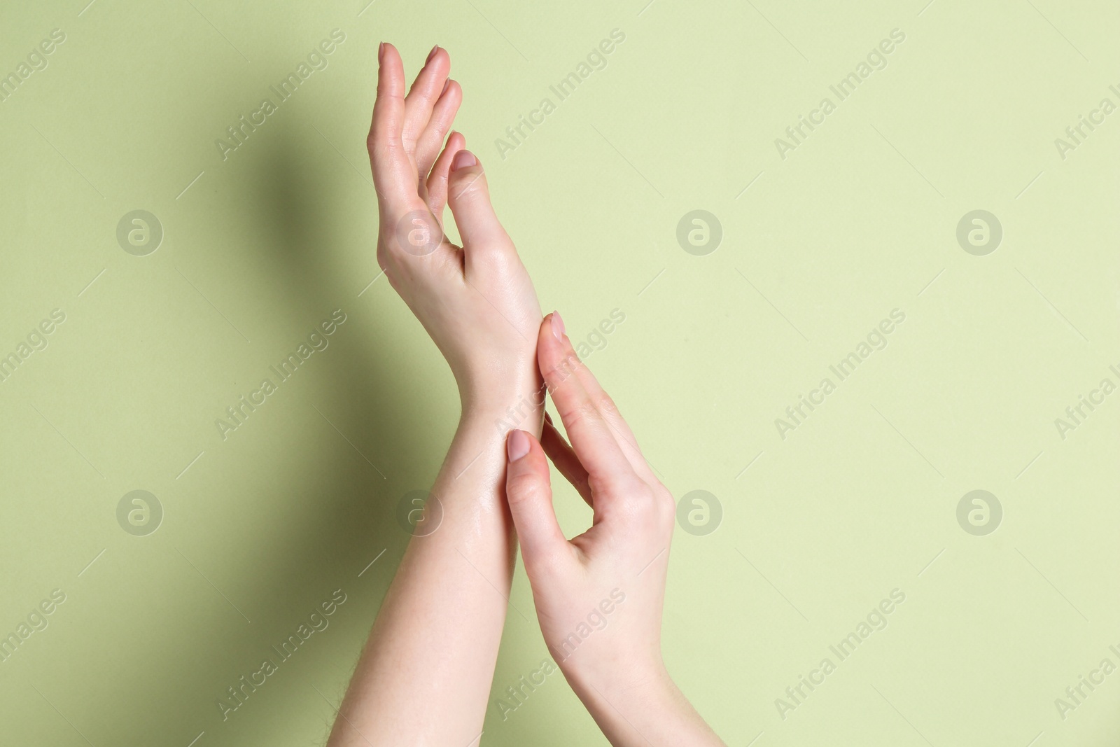 Photo of Woman applying cream on her hand against green background, closeup