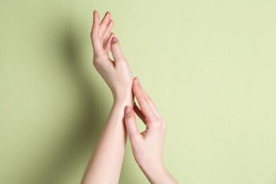 Woman applying cream on her hand against green background, closeup