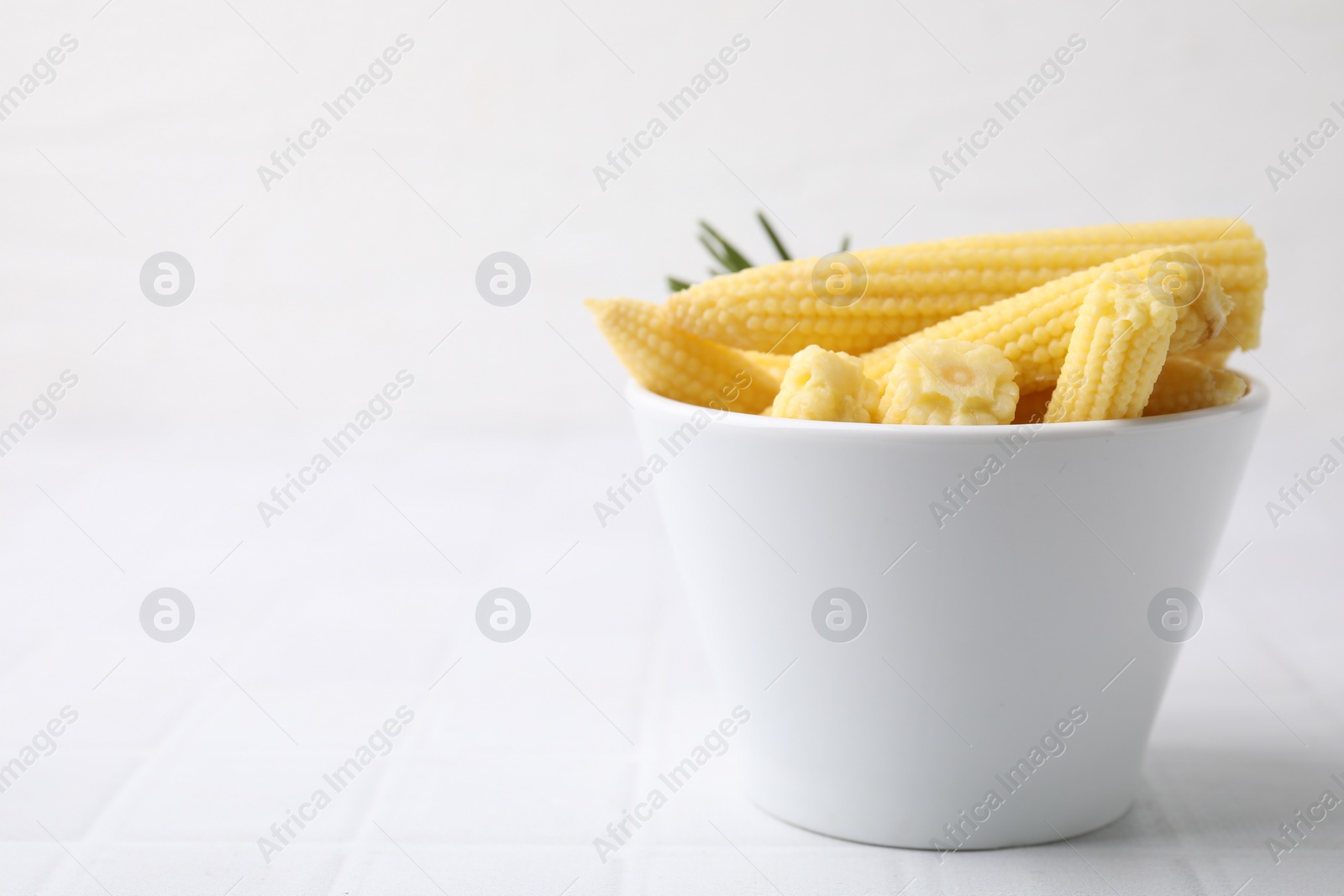 Photo of Tasty fresh yellow baby corns in bowl on white tiled table, space for text