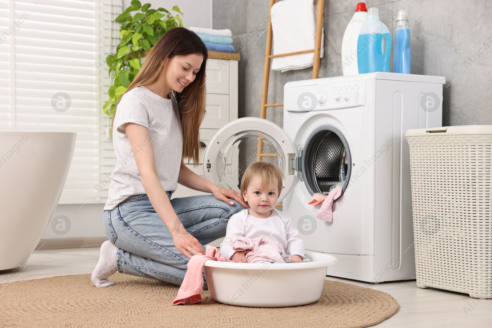 Photo of Happy mother with her daughter having fun while washing baby clothes in bathroom