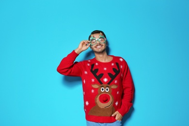 Young man in Christmas sweater with party glasses on color background