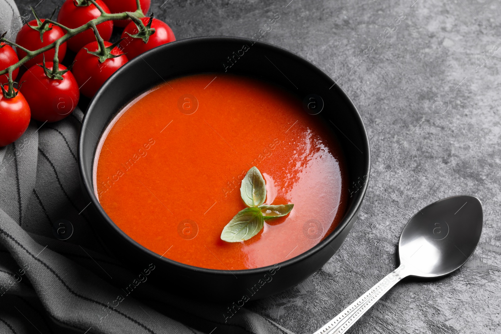 Photo of Delicious tomato cream soup in bowl served on dark textured table, closeup