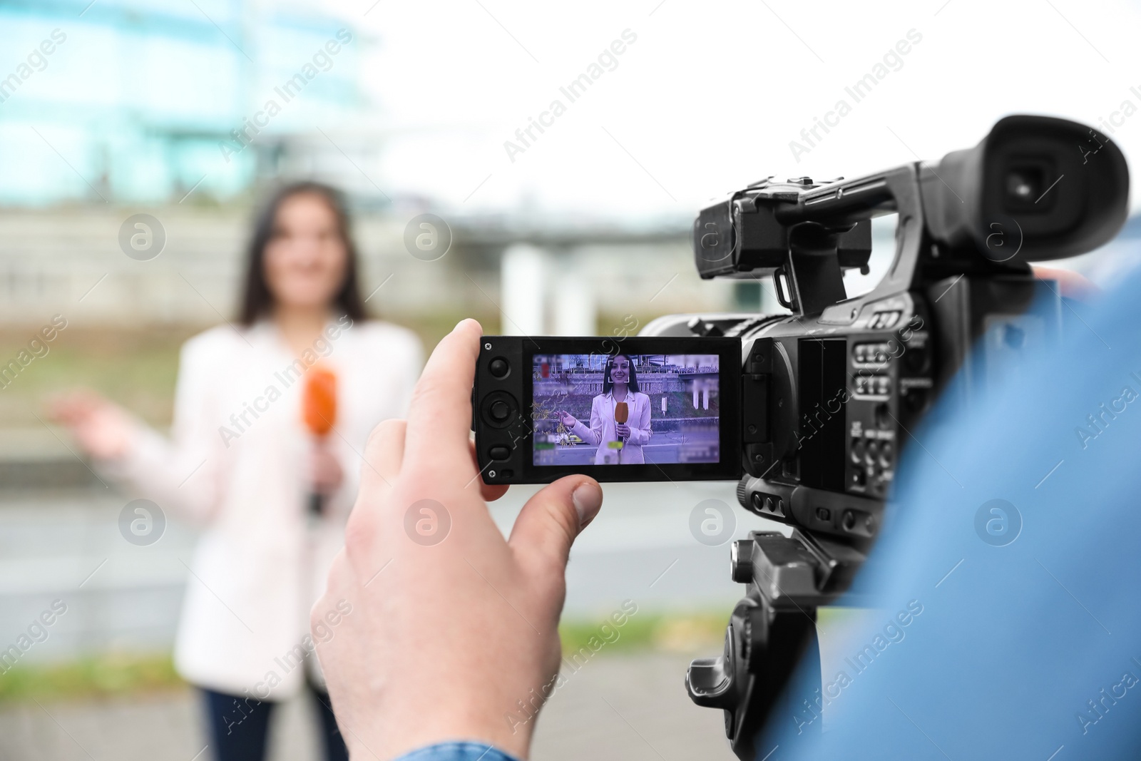 Photo of Young male journalist and video operator working on city street, focus on camera display