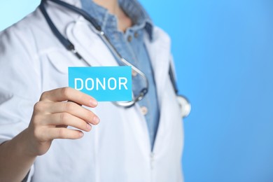 Doctor holding card with word DONOR on light blue background, closeup