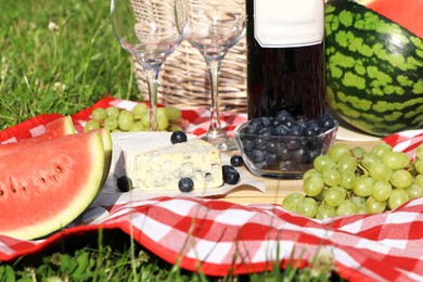 Picnic blanket with delicious food and wine outdoors on sunny day, closeup