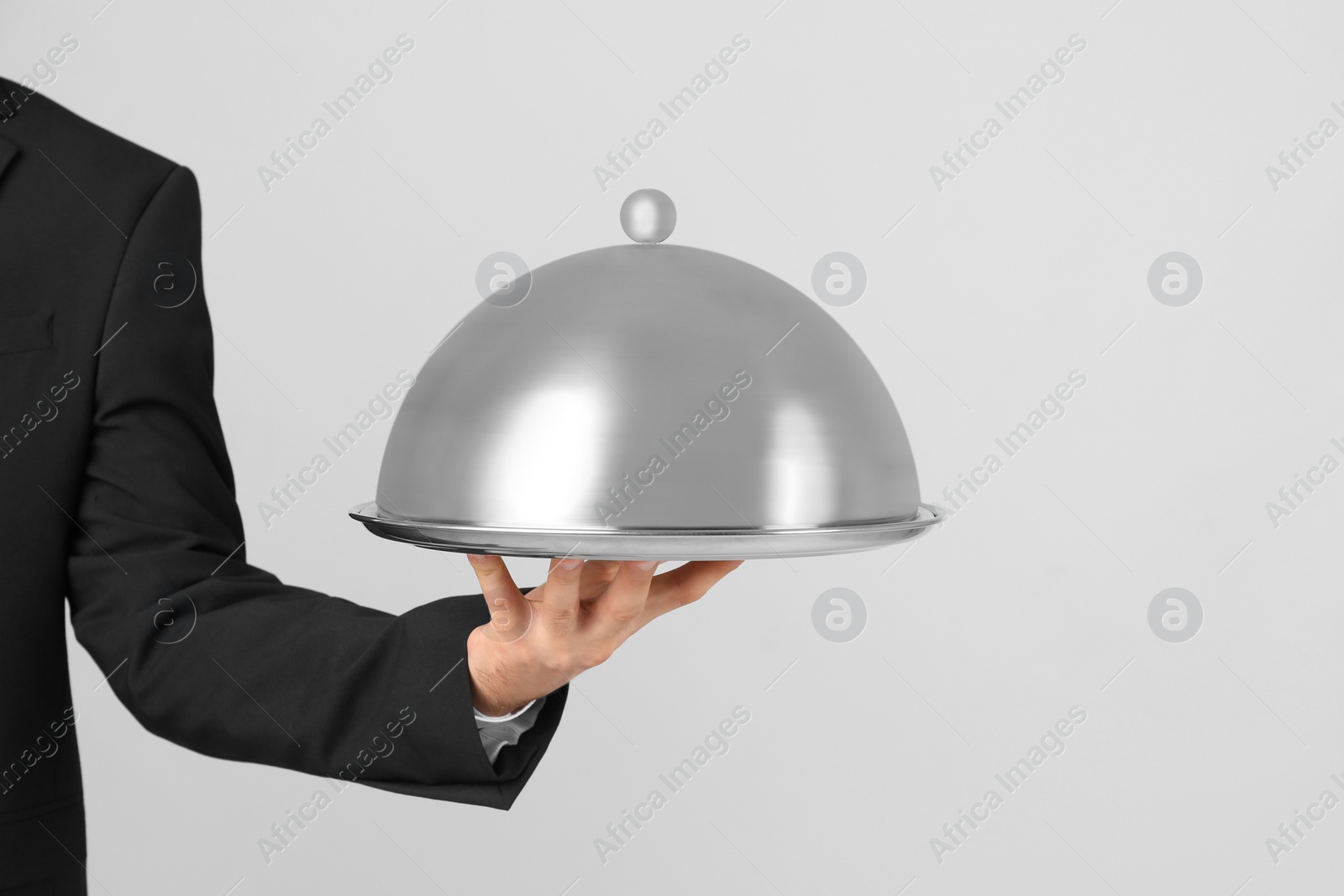 Photo of Waiter holding metal tray with lid on light background