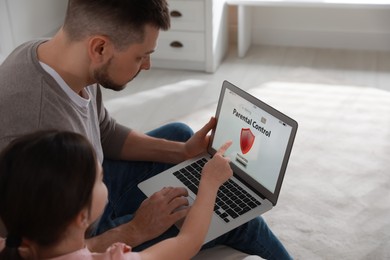 Photo of Dad installing parental control on laptop at home. Child safety