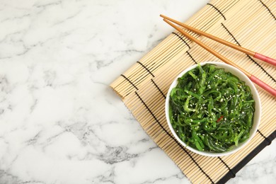 Photo of Japanese seaweed salad served on white marble table, flat lay. Space for text