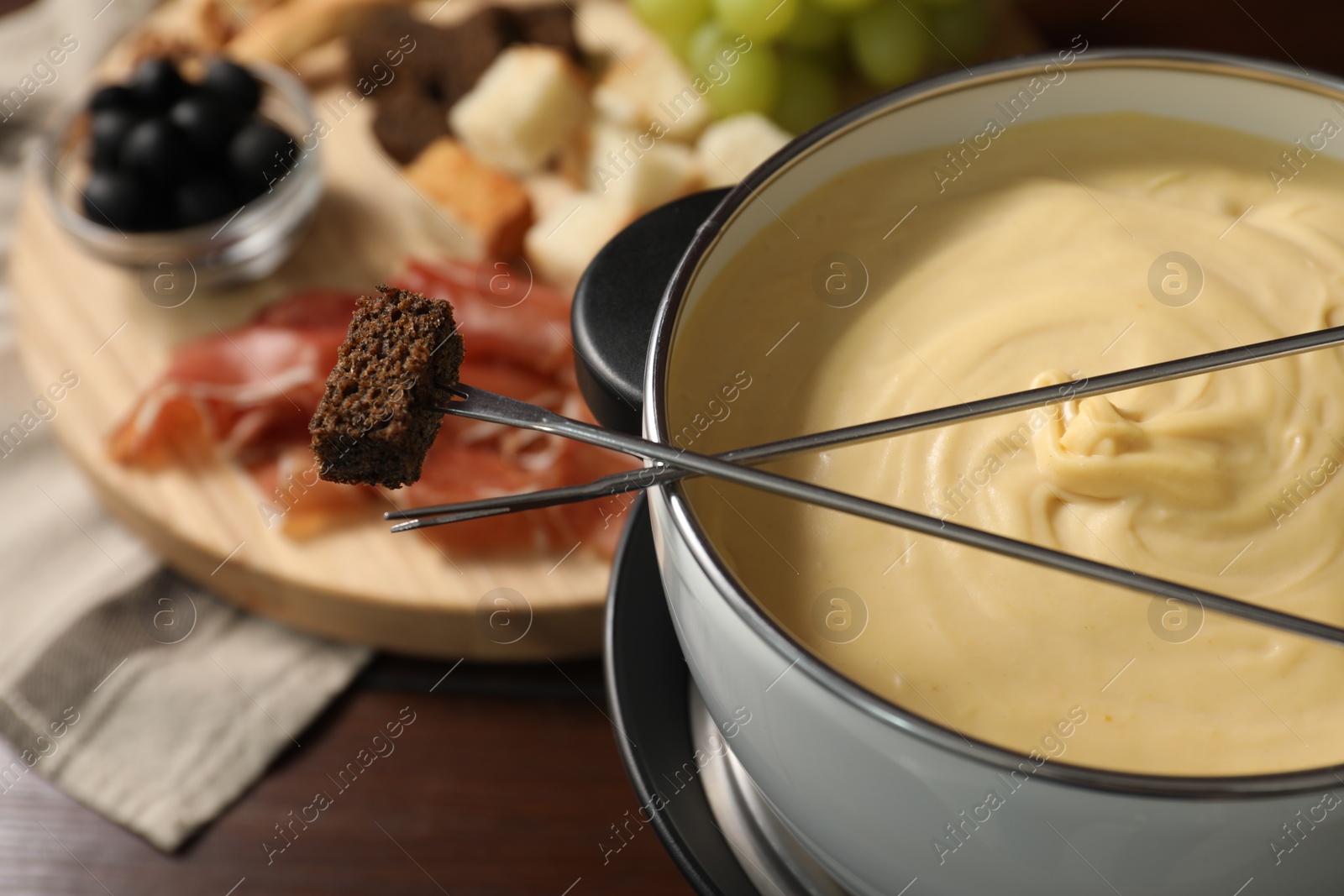 Photo of Fondue with tasty melted cheese, forks and piece of bread on wooden table, closeup