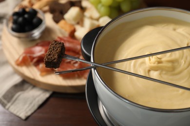 Photo of Fondue with tasty melted cheese, forks and piece of bread on wooden table, closeup