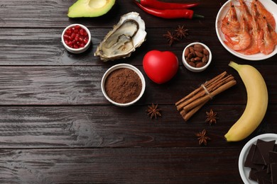 Photo of Natural aphrodisiac. Different food products and red decorative heart on dark wooden table, flat lay. Space for text