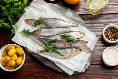 Fresh raw sprats, dill and other products on wooden table, flat lay