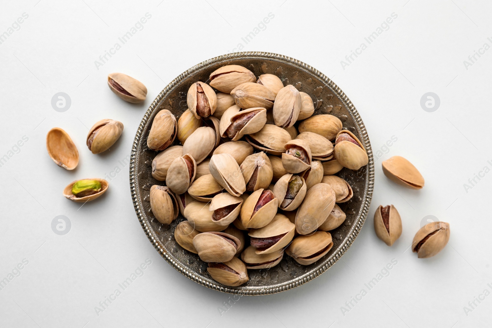 Photo of Plate and pistachio nuts on white background, flat lay