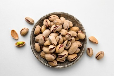 Plate and pistachio nuts on white background, flat lay