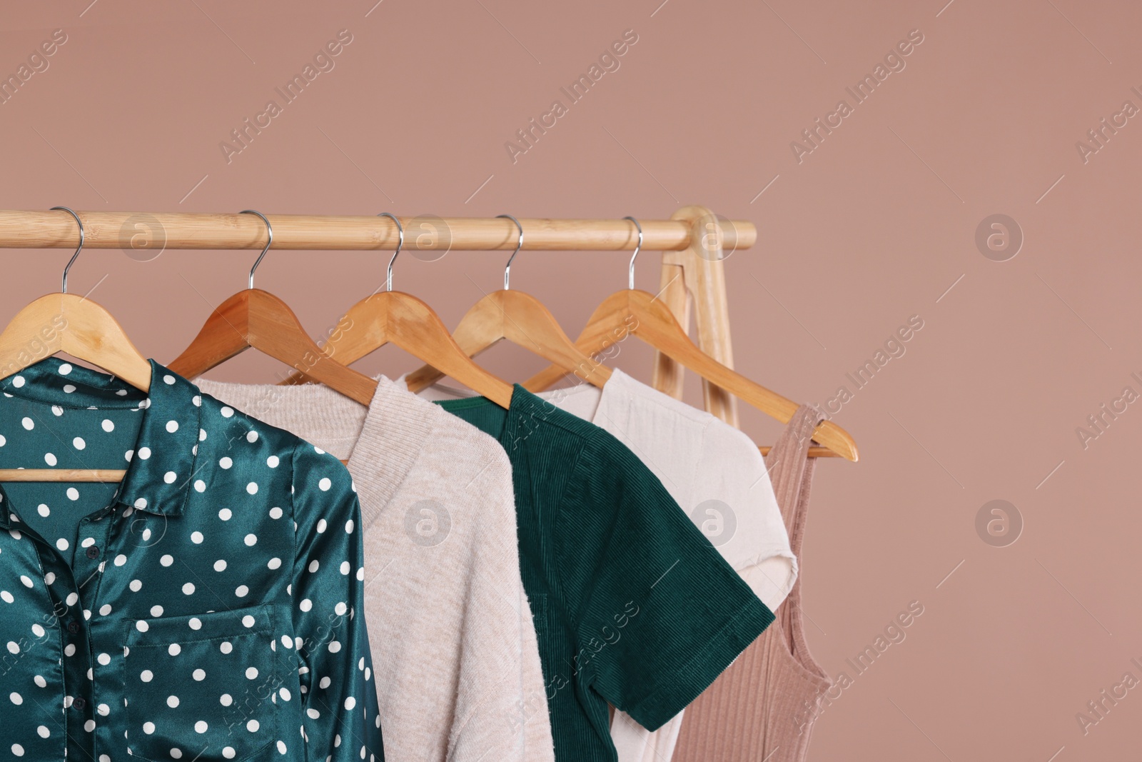 Photo of Rack with stylish women`s clothes on wooden hangers against beige background, space for text