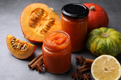 Jars of pumpkin jam and ingredients on grey table