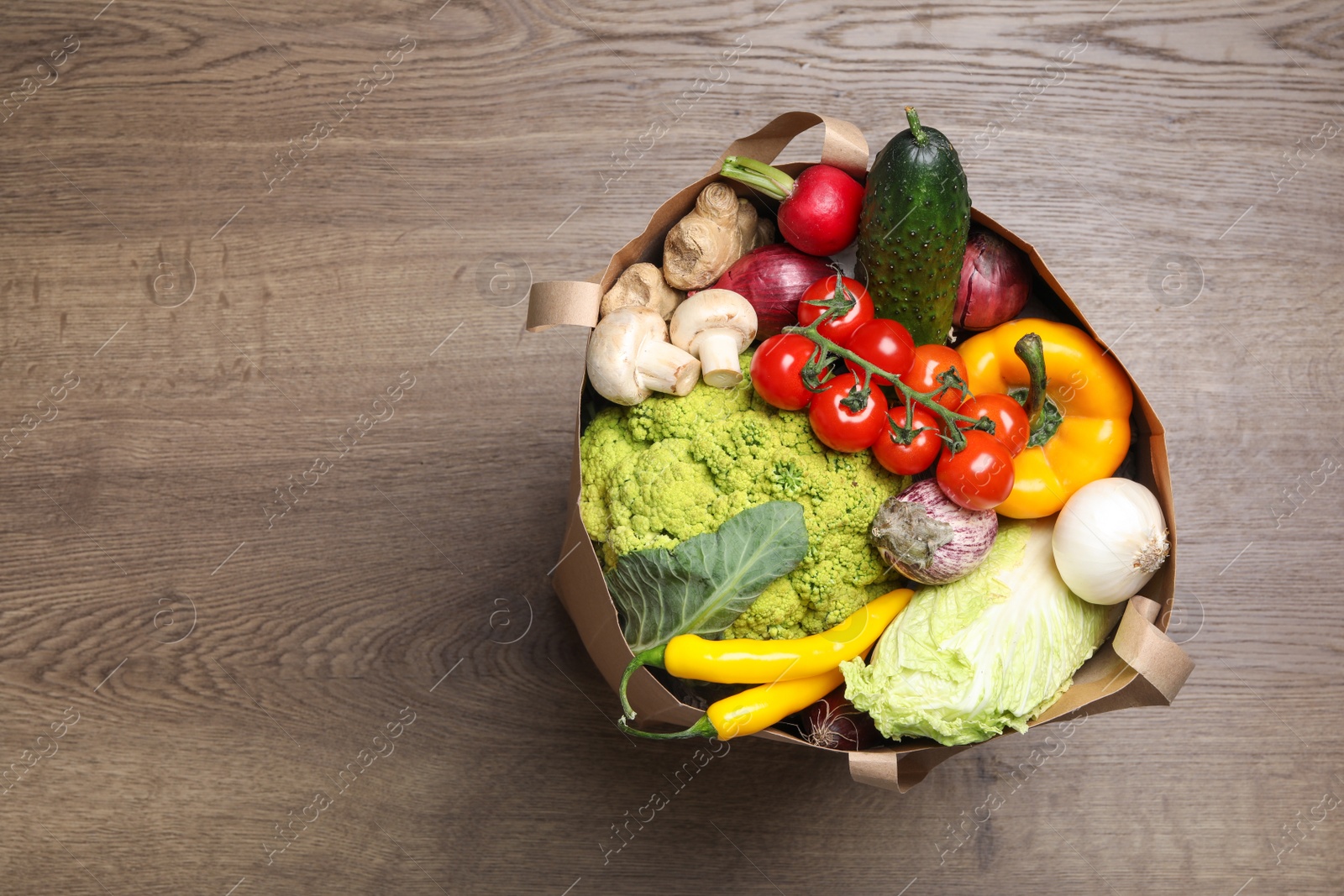 Photo of Paper bag full of fresh vegetables on wooden background, top view. Space for text