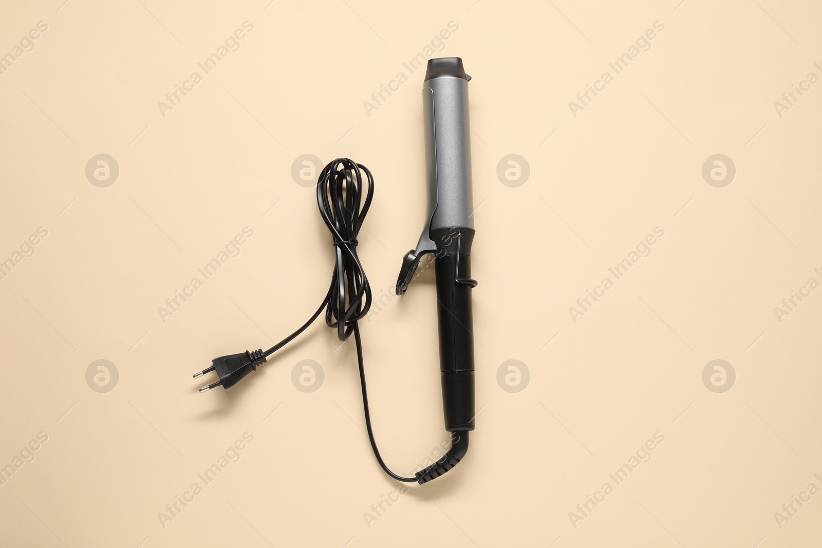 Photo of Curling iron on beige background, top view