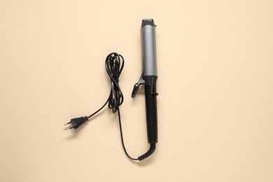 Curling iron on beige background, top view