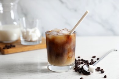 Photo of Refreshing iced coffee with milk in glass, beans, spoon and sugar cube on white wooden table