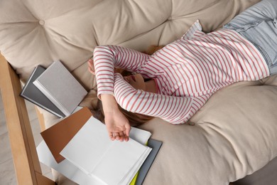Photo of Young tired woman sleeping near books on couch