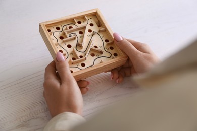 Woman holding wooden toy maze with metal ball at table, closeup