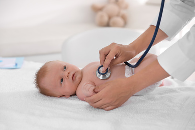 Photo of Doctor examining cute baby with stethoscope indoors, closeup. Health care