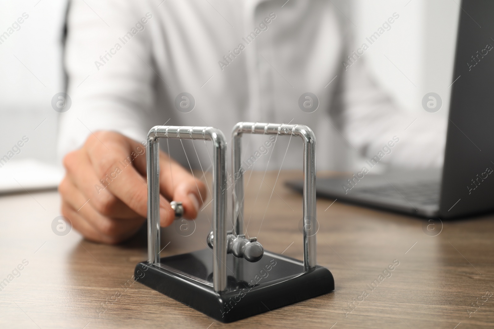 Photo of Man playing with Newton's cradle at office table, closeup. Physics law of energy conservation