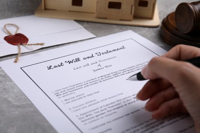 Photo of Woman signing last will and testament at light grey table, closeup