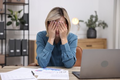 Photo of Overwhelmed woman sitting at table with laptop and documents in office