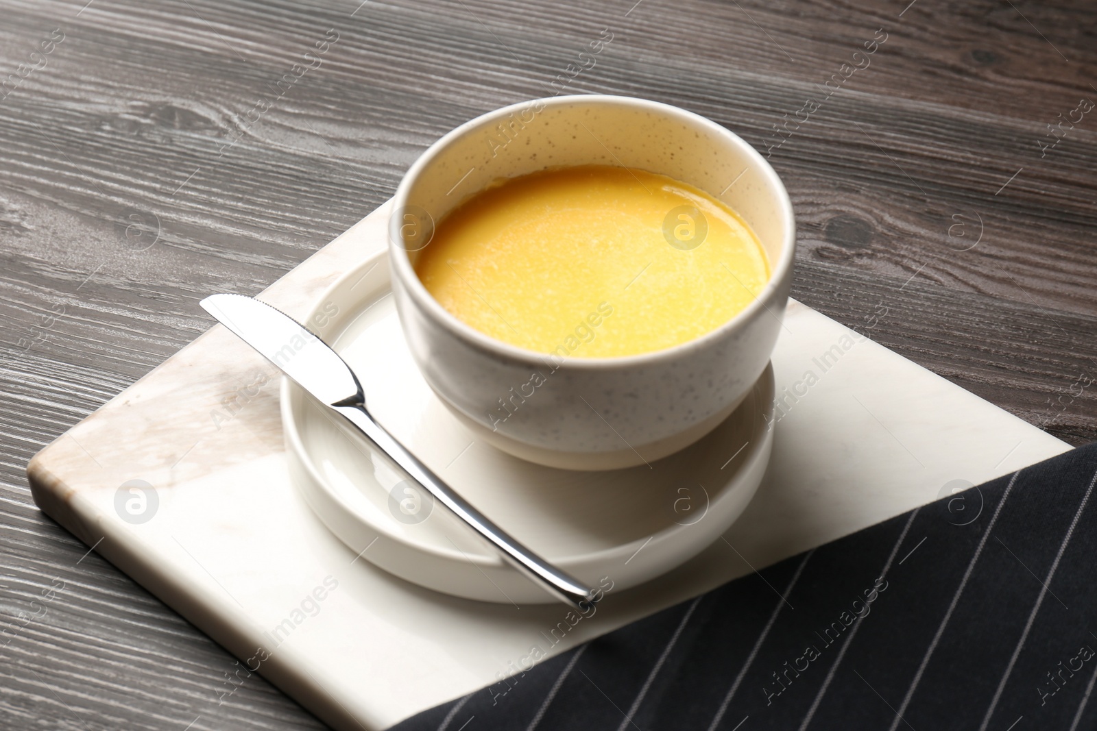 Photo of Bowl of melting butter served on wooden table