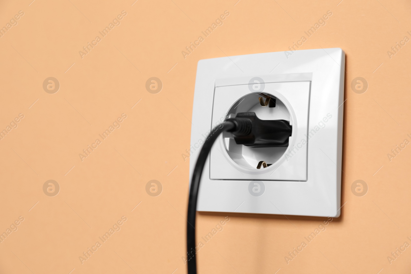 Photo of Power socket with inserted plug on pale orange wall, space for text. Electrical supply
