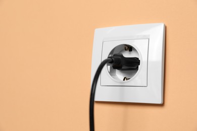 Power socket with inserted plug on pale orange wall, space for text. Electrical supply