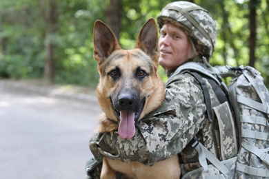 Photo of Man in military uniform with German shepherd dog, outdoors