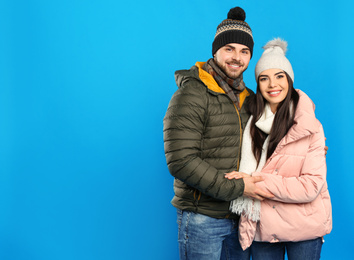 Photo of Happy young couple in warm clothes on blue background, space for text. Winter vacation