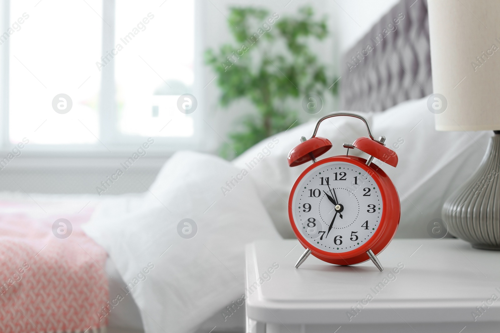 Photo of Analog alarm clock on table in bedroom. Time of day