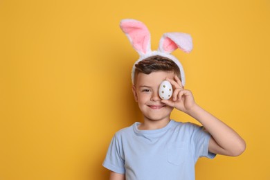 Cute little boy in bunny ears holding Easter egg on yellow background. Space for text