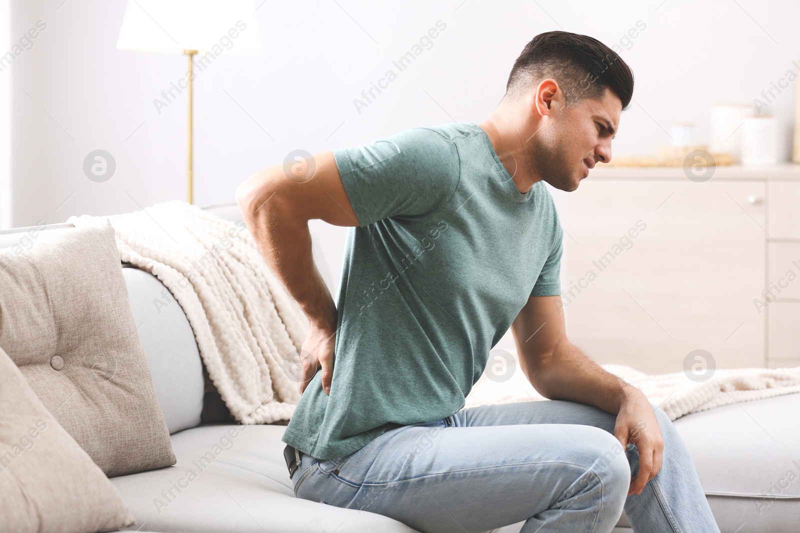 Photo of Man suffering from back pain at home. Bad posture problem