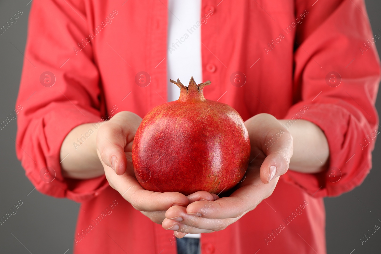 Photo of Woman holding whole pomegranate on grey background, closeup