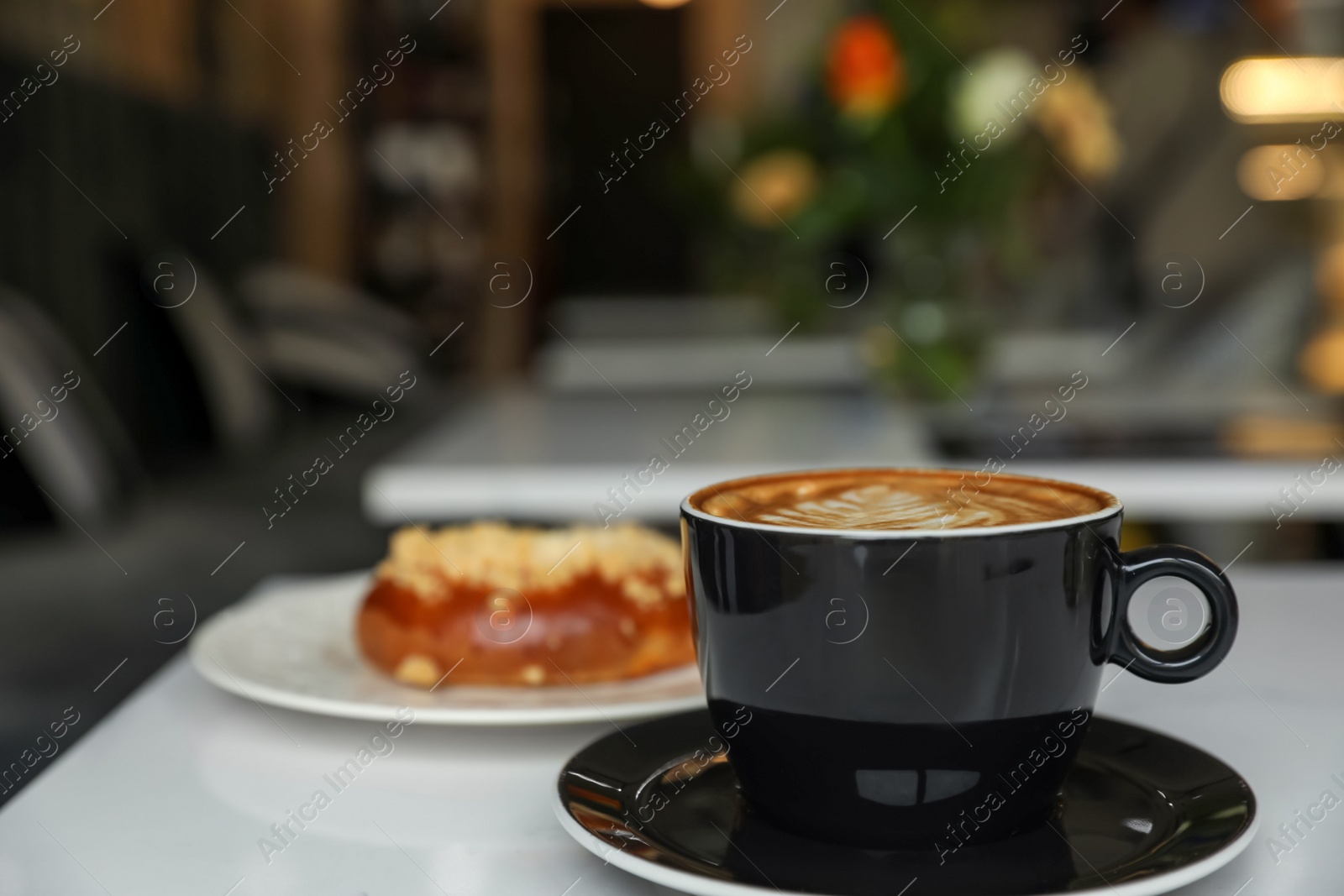 Photo of Cup of fresh coffee and bun on table in cafeteria