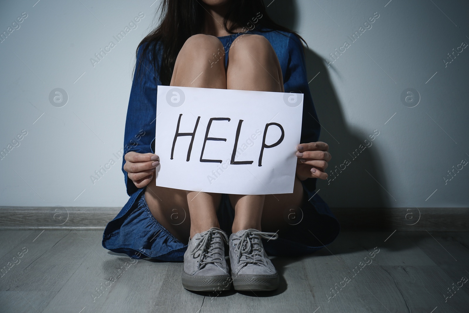 Photo of Young woman with sign HELP near white wall, closeup. Domestic violence concept