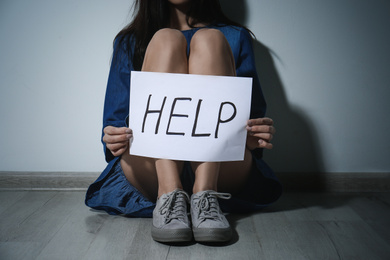 Young woman with sign HELP near white wall, closeup. Domestic violence concept