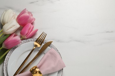 Stylish table setting with cutlery and tulips on white marble background, flat lay. Space for text