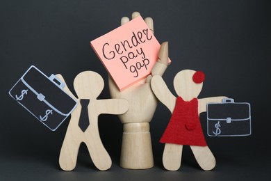 Gender pay gap. Wooden mannequin hand with paper note, figures of man and woman on black background